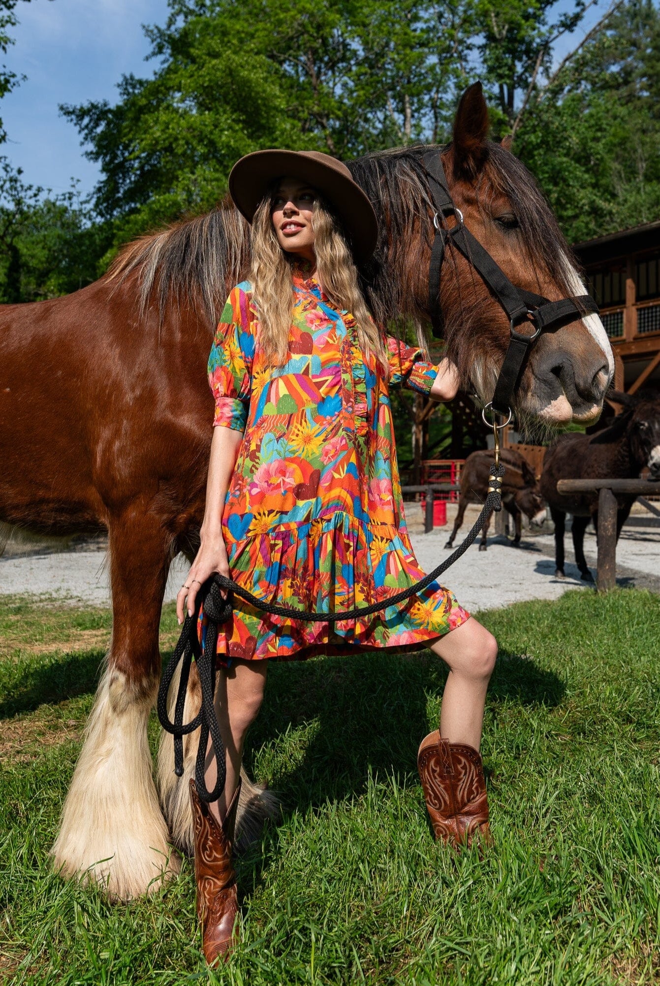 Woman in a colorful dress standing next to a horse in an outdoor setting with trees and buildings in the background.