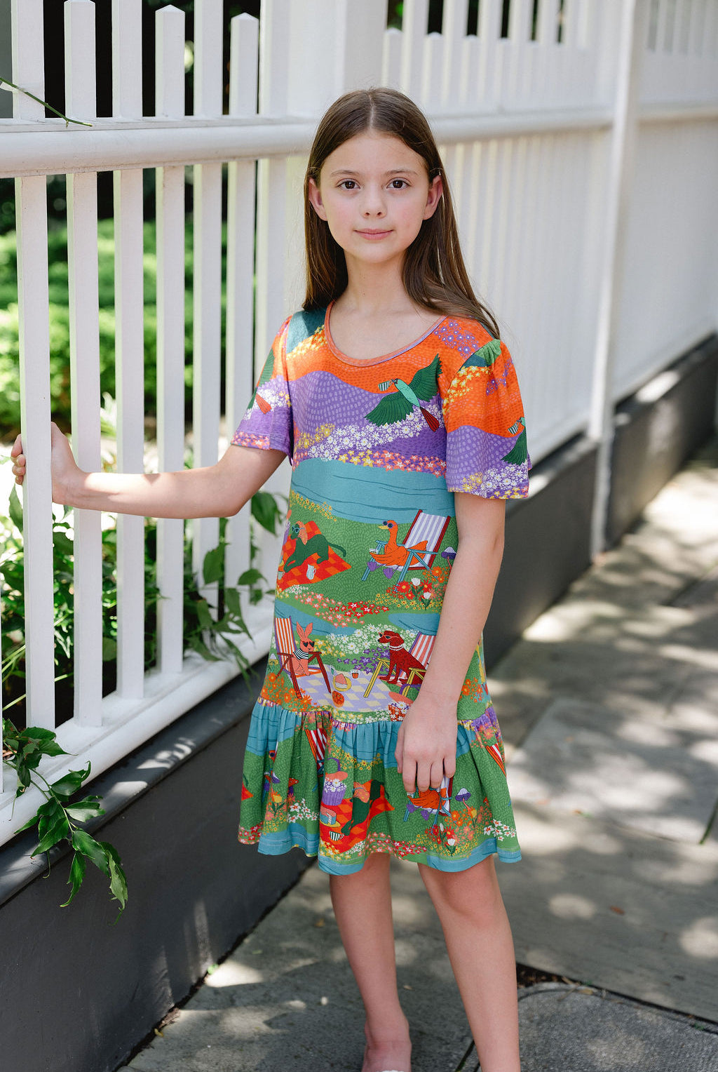 Girls colorful Victoria Knit Dress featuring a whimsical scenic print with flutter sleeves and a tiered skirt.