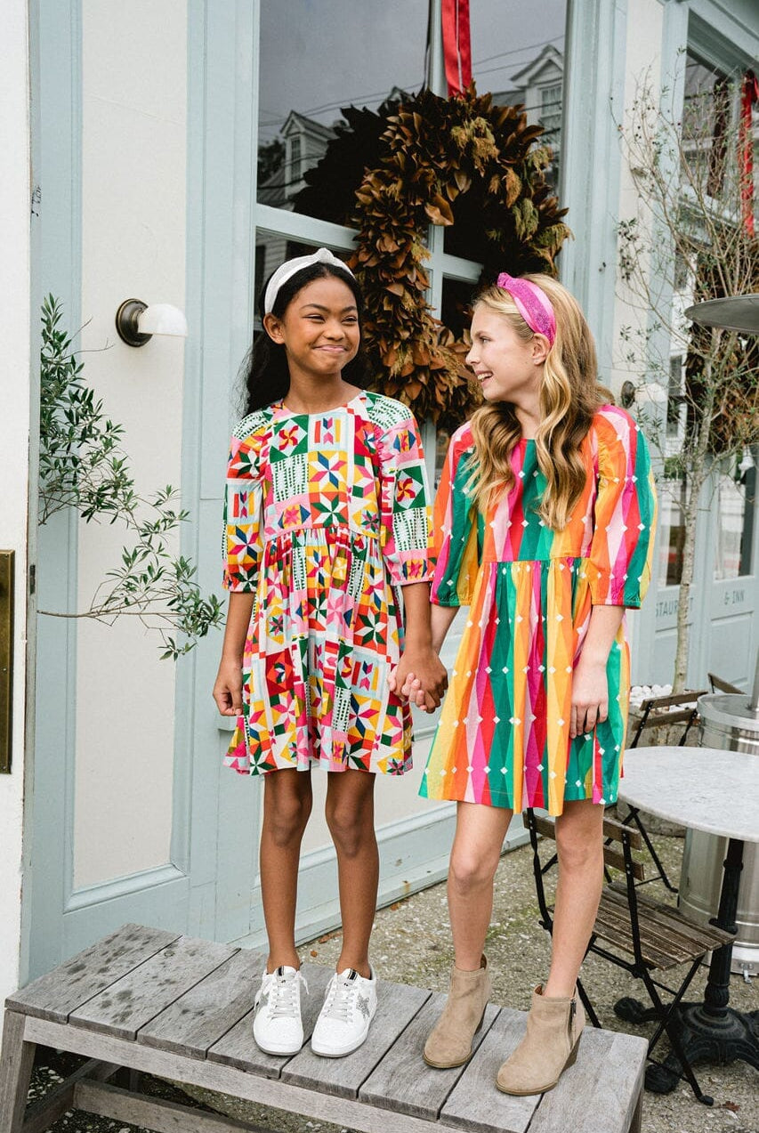 Two girls holding hands while wearing dresses.