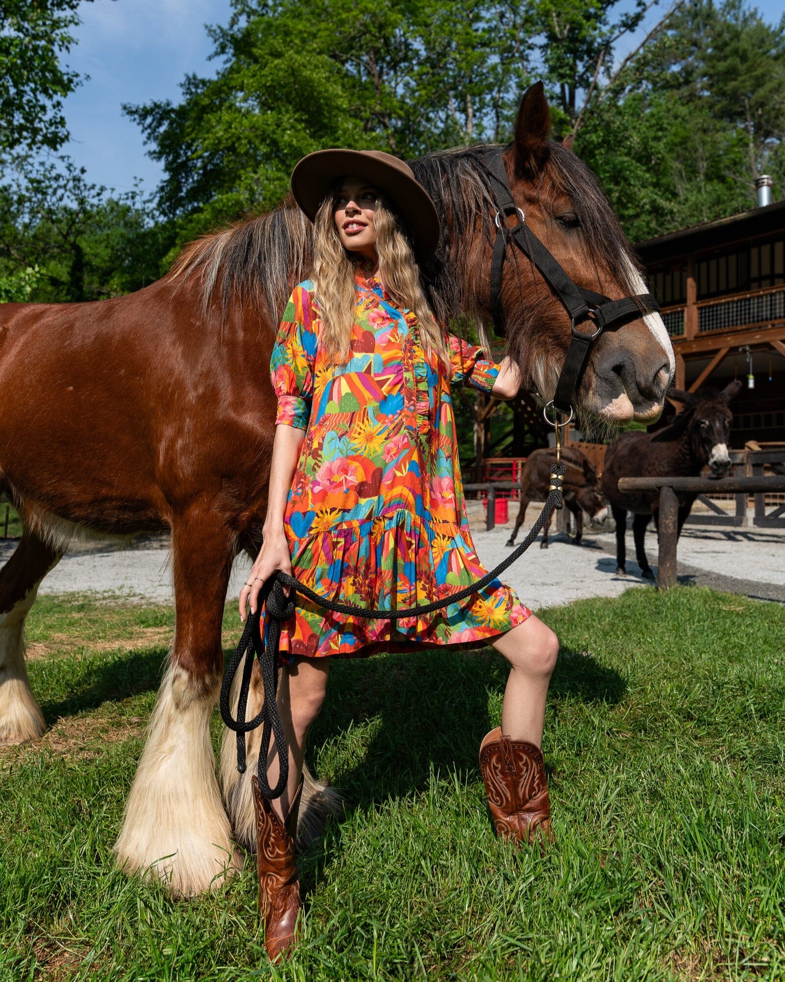 Woman in a colorful dress standing next to a horse in an outdoor setting with trees and buildings in the background.