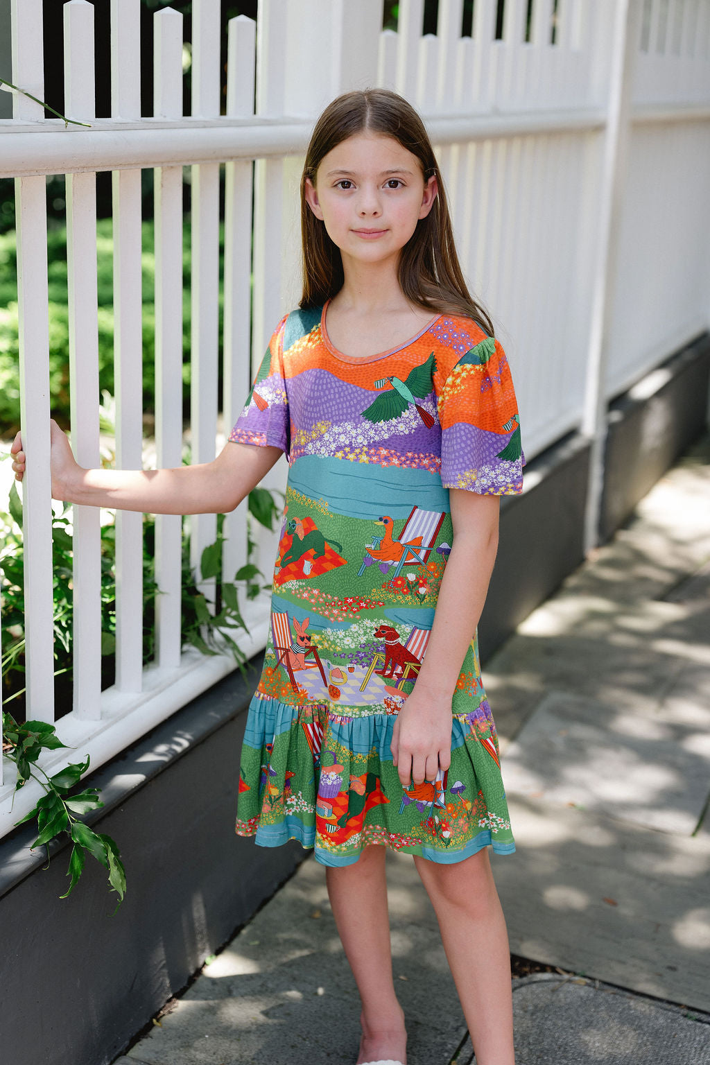 Girls colorful Victoria Knit Dress featuring a whimsical scenic print with flutter sleeves and a tiered skirt.