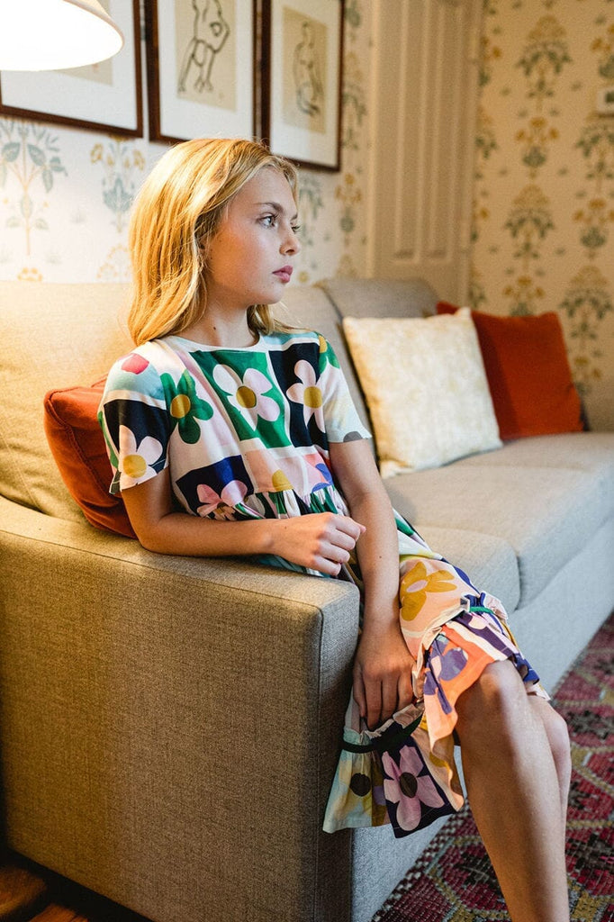 Girl sitting down while wearing the Ollie Flower Power dress.